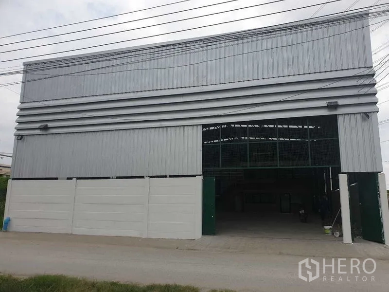 Warehouse for rent in Prawet, Bangkok - Front facade of the warehouse with a large sliding entrance gate and driveway.