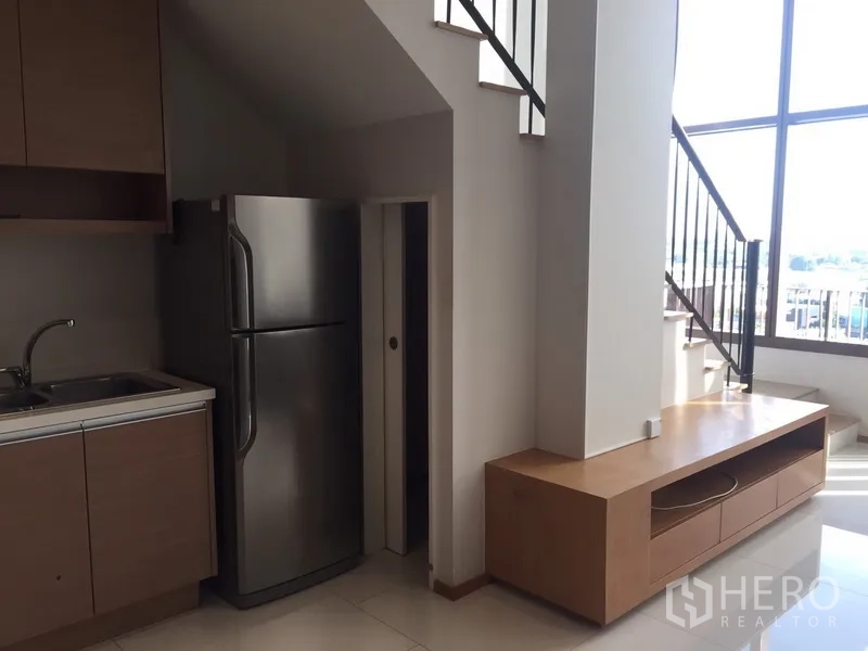 Condominium for rent in Khlong Toei, Bangkok - Kitchen corner and under-stair storage next to a low TV console and tall windows.