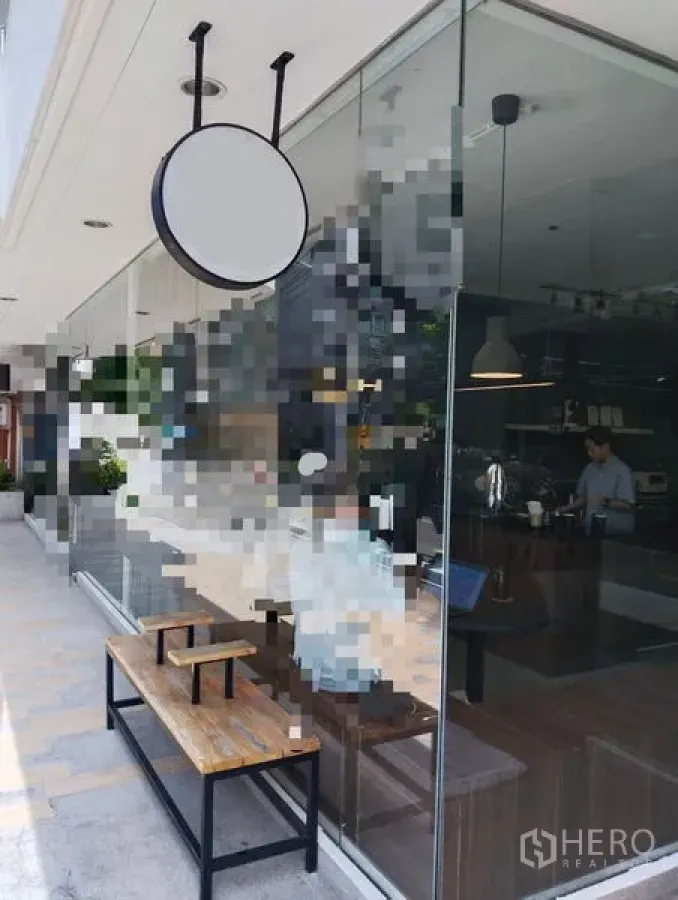 Retail Space for rent in Watthana, Bangkok - Street-facing glass storefront with round hanging sign and wooden bench along the sidewalk.