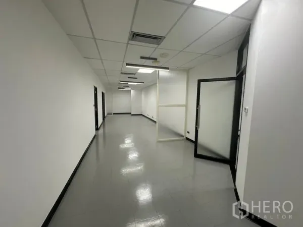 办公空间 出租 - 带吊顶灯光的长形工作走廊，配有磨砂玻璃隔断与开启的门。