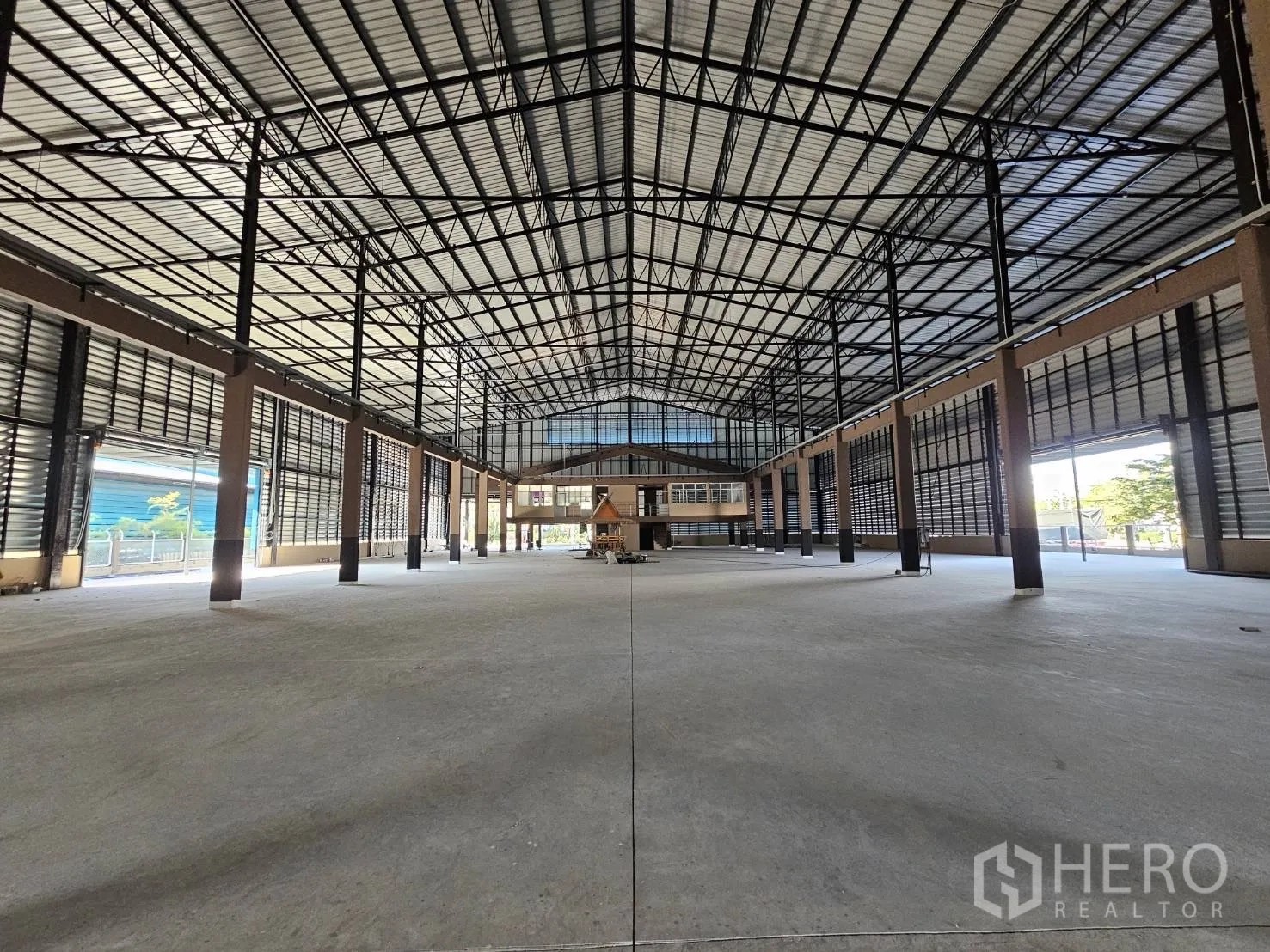 Factory for rent in Chon Buri - Central aisle view of the factory floor with open space and a glass-fronted office block.