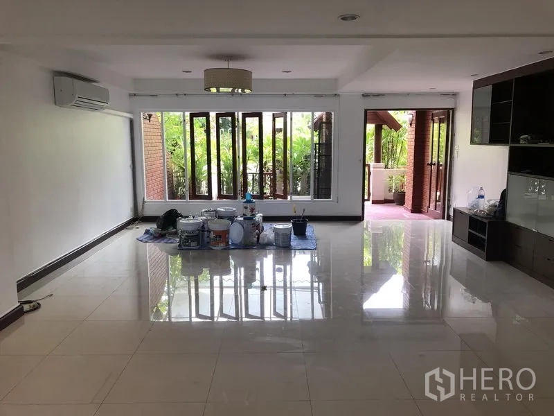 Townhouse for rent or sale in Watthana, Bangkok - Bright living room with glossy tile floors, wall-to-wall windows and access to a covered terrace.