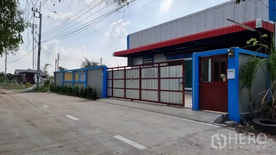 货栈 出租在Min Buri, Bangkok - 独立仓库的大门，红色雨棚、蓝色外墙及宽阔的混凝土车道。