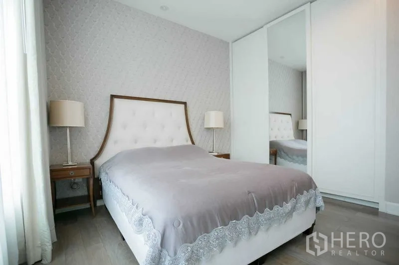 Condominium for rent or sale in Pathum Wan, Bangkok - Cozy bedroom with upholstered headboard, bedside lamps and mirrored wardrobe.