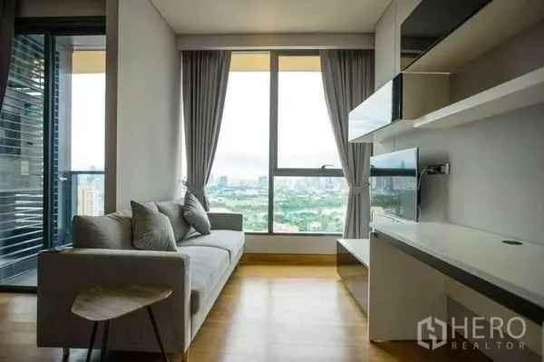 Condominium for rent in Khlong Toei, Bangkok - Bright living room with sofa, balcony access and wide city skyline view through big windows.