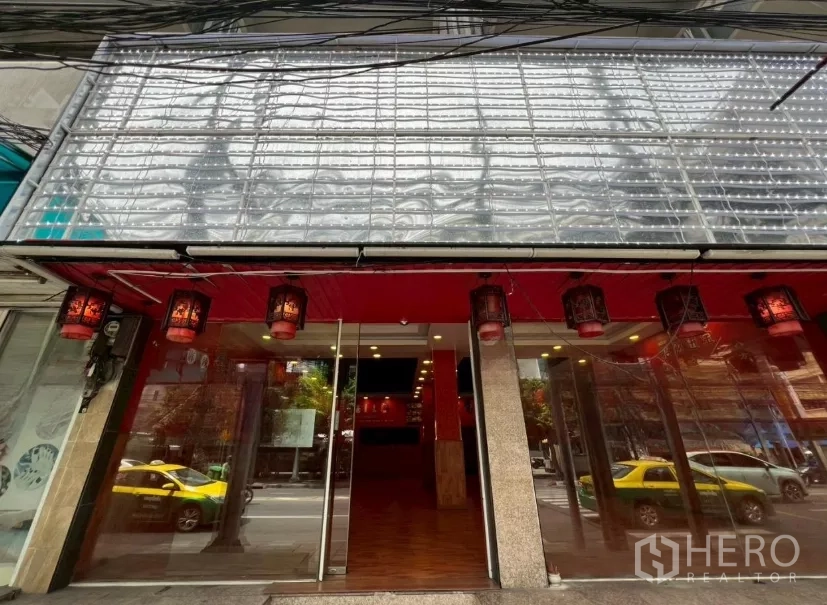 Shophouse for rent in Watthana, Bangkok - Street-level shophouse facade with wide glass entrance and red lanterns on a busy road.