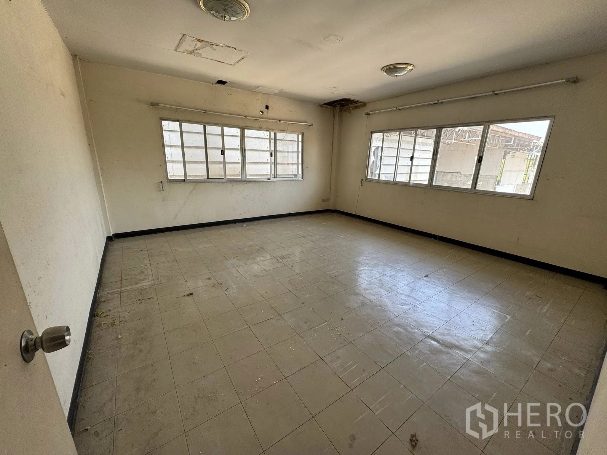 Warehouse for rent in Mueang Samut Sakhon, Samut Sakhon - Bright corner office with windows on two sides and a scuffed tiled floor.