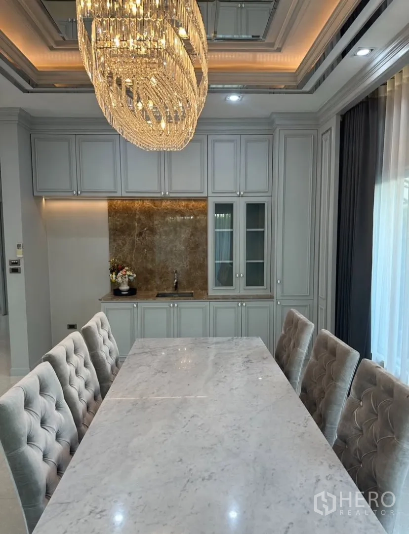 Detached House for rent or sale in Prawet, Bangkok - Dining space with marble tabletop, tufted chairs, and built-in cabinetry with a wet bar.