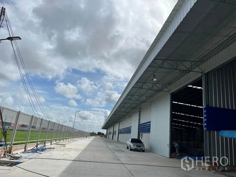 货栈 出租在Lat Krabang, Bangkok - 叻甲挽现代仓库外观，宽阔混凝土车道、装卸口与安防围栏，天空多云。
