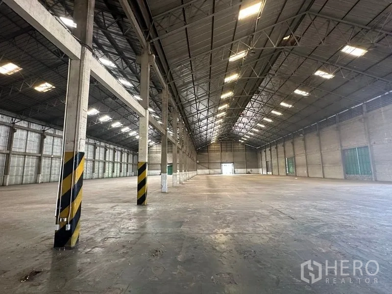 Warehouse for rent in Mueang Pathum Thani, Pathum Thani - Open storage area with concrete columns marked with safety stripes and expansive slab floor.