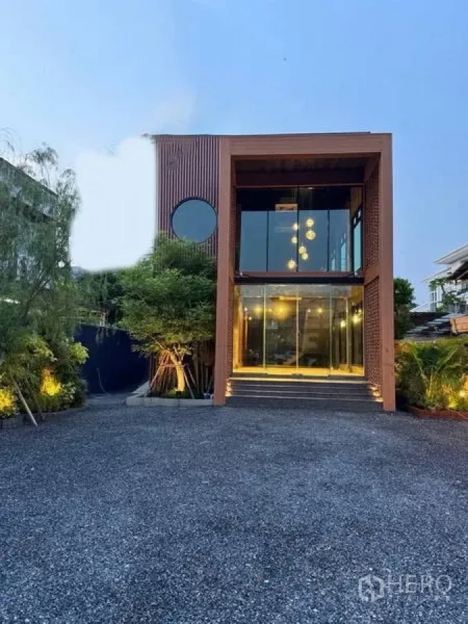 Standalone for rent in Sathon, Bangkok - Modern standalone building exterior with floor-to-ceiling glass facade, bold cube frame, landscaping and a wide gravel parking forecourt.