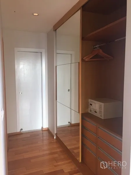 Condominium for rent in Khlong Toei, Bangkok - Hallway walk-in closet with mirrored sliding wardrobe, drawers and a safe on wooden flooring.