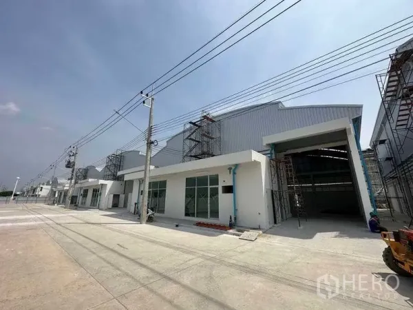 Factory for rent in Khlong Luang, Pathum Thani - Row of newly built factory units along a wide access road with power lines overhead.
