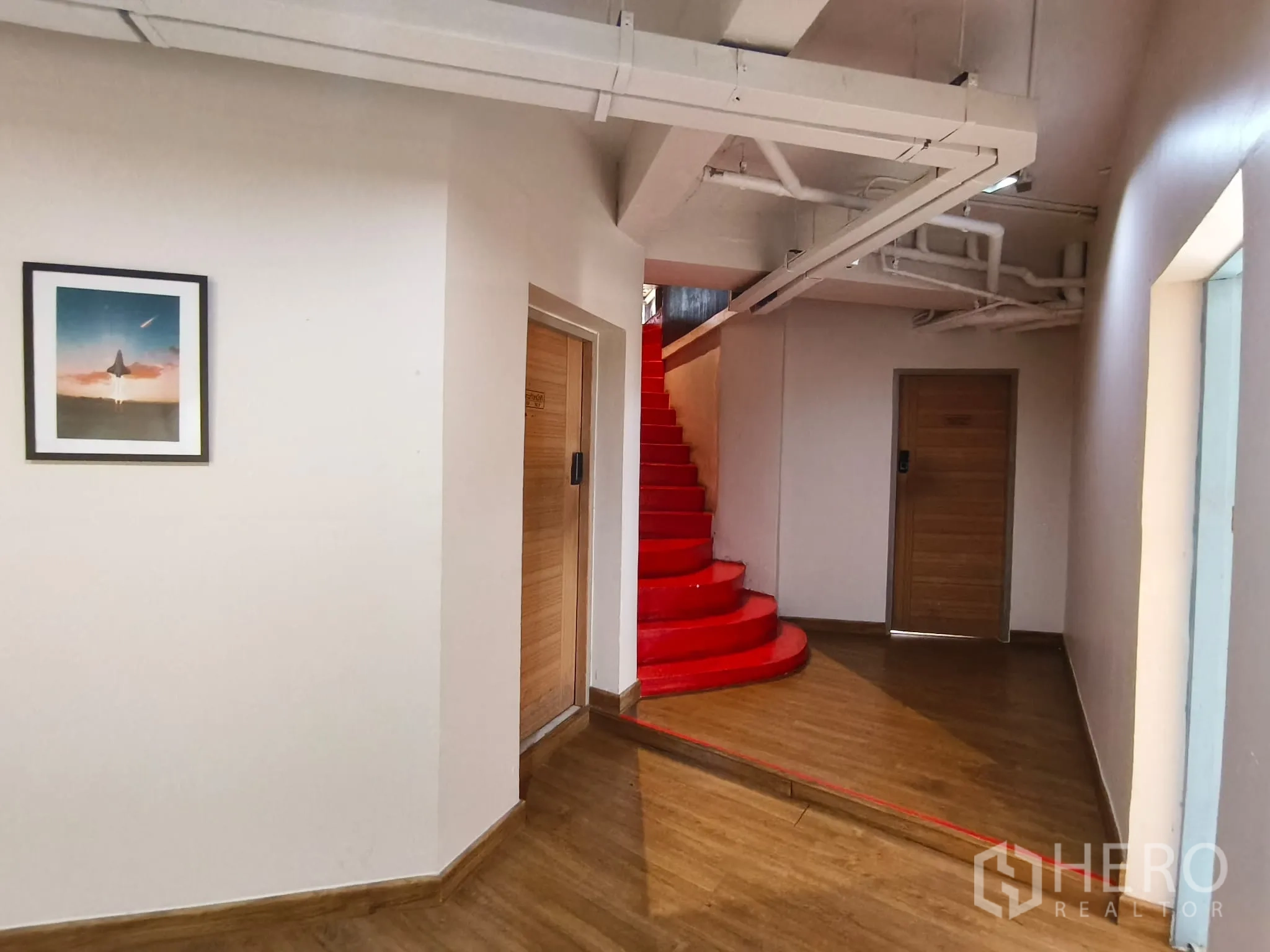 Shophouse for rent in Watthana, Bangkok - Hallway with a bold red spiral staircase and wooden doors.
