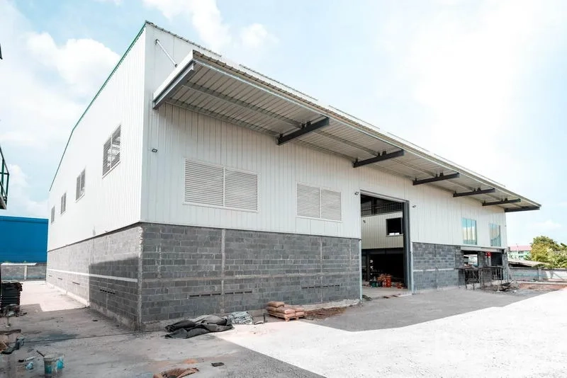 Warehouse for rent in Lat Krabang, Bangkok - Modern steel-frame warehouse exterior with high eaves, louvered vents and a large loading bay on a concrete yard.
