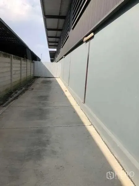 Warehouse for rent in Bang Phli, Samut Prakan - Side driveway with concrete paving and boundary wall running along the warehouse.