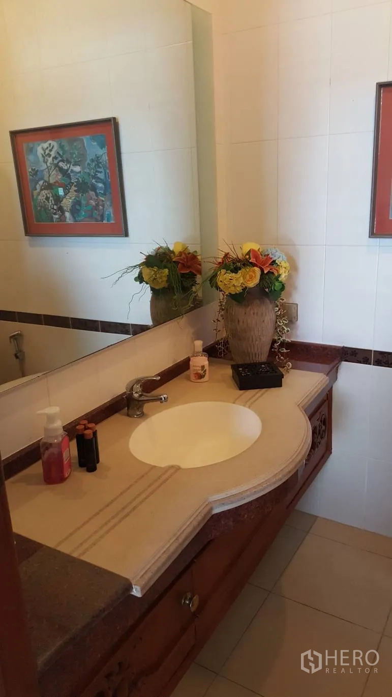 Detached House for rent in Khlong Toei, Bangkok - Tiled bathroom featuring a large mirror, stone countertop vanity and decorative flowers.