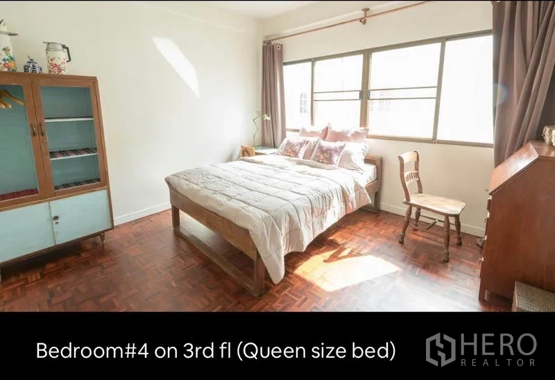 Townhouse for rent in Khlong Toei, Bangkok - Sunlit third-floor bedroom with queen-size bed, large windows and vintage cabinet.