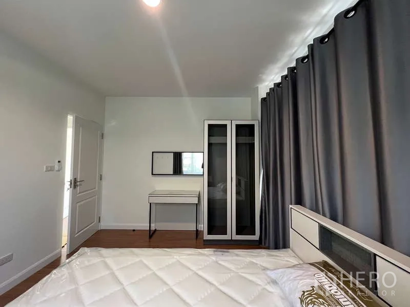 Detached House for rent in Bang Kapi, Bangkok - Bedroom view showing vanity desk and tall wardrobe next to grey curtains.