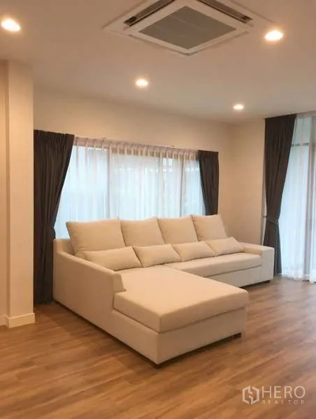 Detached House for rent in Bang Kapi, Bangkok - Airy living room with L-shaped white sofa, large windows and cassette ceiling AC.