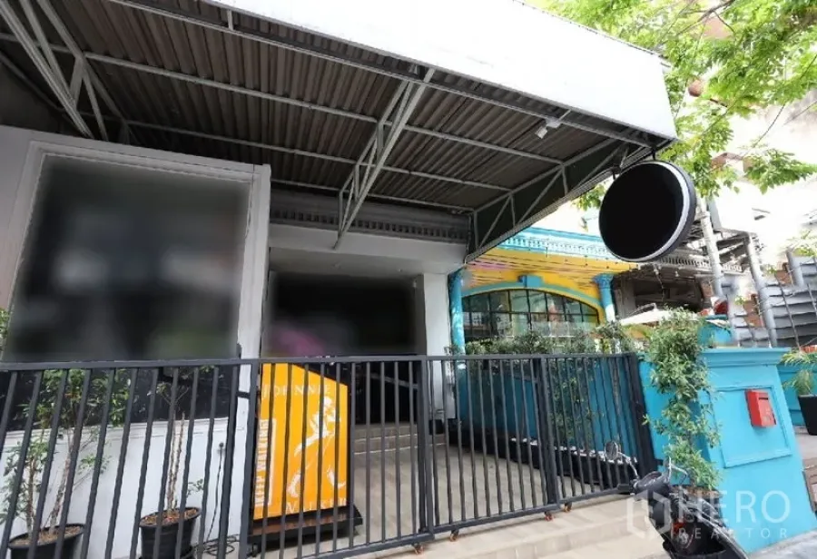 อาคารพาณิชย์ ให้เช่าหรือขายในWatthana, Bangkok - ด้านหน้าร้านพร้อมกันสาดโลหะ ป้ายกลม และรั้วเหล็ก มีต้นไม้ร่มรื่น