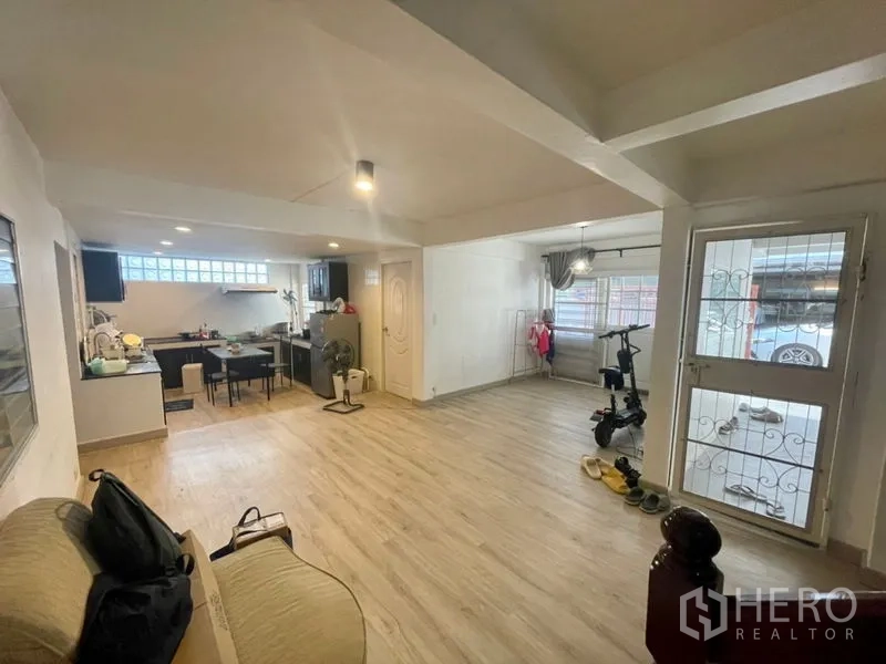 Townhouse for rent in Din Daeng, Bangkok - Spacious living room view toward the front door and window grilles beside the kitchen zone.