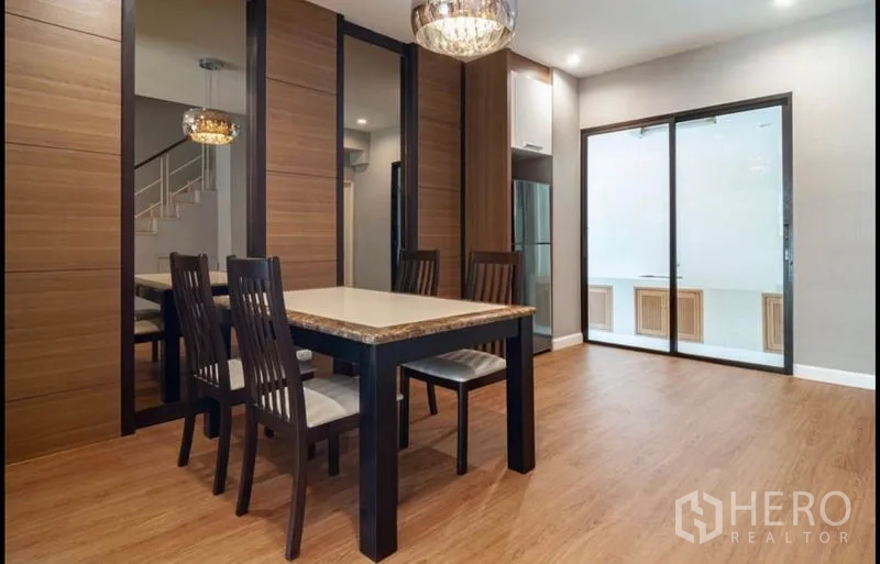 Townhouse for sale in Khlong Toei, Bangkok - Dining area with chandelier, marble-top table, wood wall panels, mirrors and sliding glass doors to pantry.