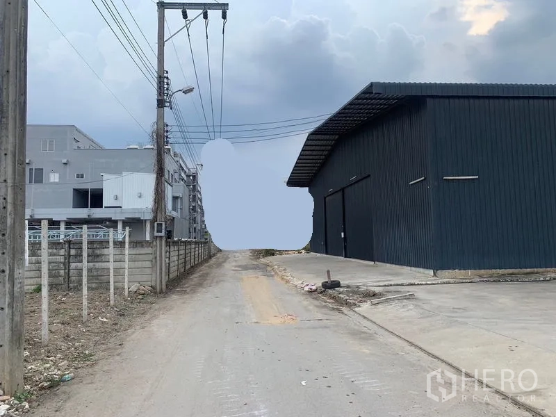Warehouse for rent in Khan Na Yao, Bangkok - Narrow access road beside the warehouse with power lines and a concrete apron for truck entry.
