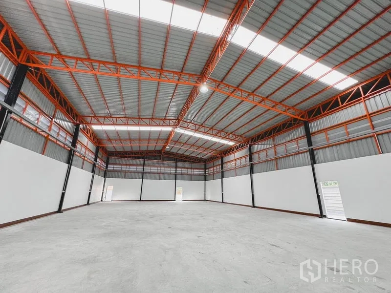 Warehouse for rent or sale in Khlong Luang, Pathum Thani - Spacious warehouse interior with high gabled steel roof, orange trusses and polished concrete floor.