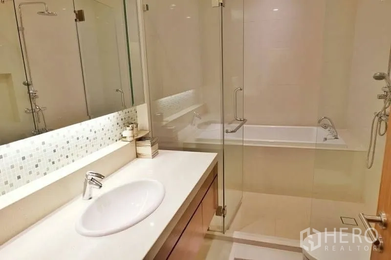 Condominium for rent in Khlong Toei, Bangkok - Bathroom with illuminated vanity, glass shower enclosure and separate bathtub.