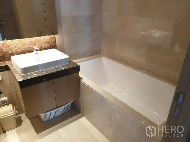 Condominium for rent in Pathum Wan, Bangkok - Contemporary bathroom with bathtub, marble-top vanity and warm lighting.