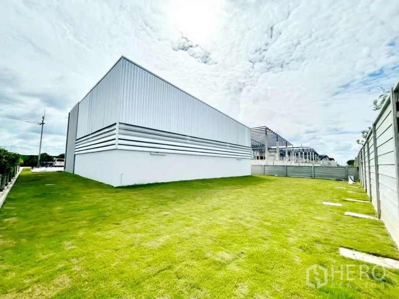 Warehouse for sale in Lam Luk Ka, Pathum Thani - Side lawn and perimeter wall behind the warehouse offering outdoor storage or future expansion.