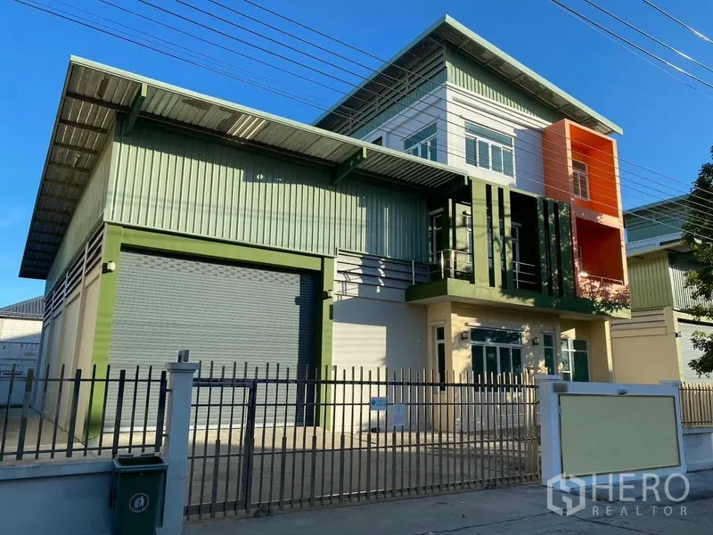 Factory for rent or sale in Lam Luk Ka, Pathum Thani - Modern factory exterior in Lam Luk Ka with green metal cladding, large roller shutter, office block and gated fence.
