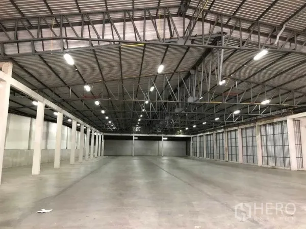 Warehouse for rent in Pak Kret, Nonthaburi - Wide column-free warehouse bay with multiple roller shutter loading doors and high ceiling lights.