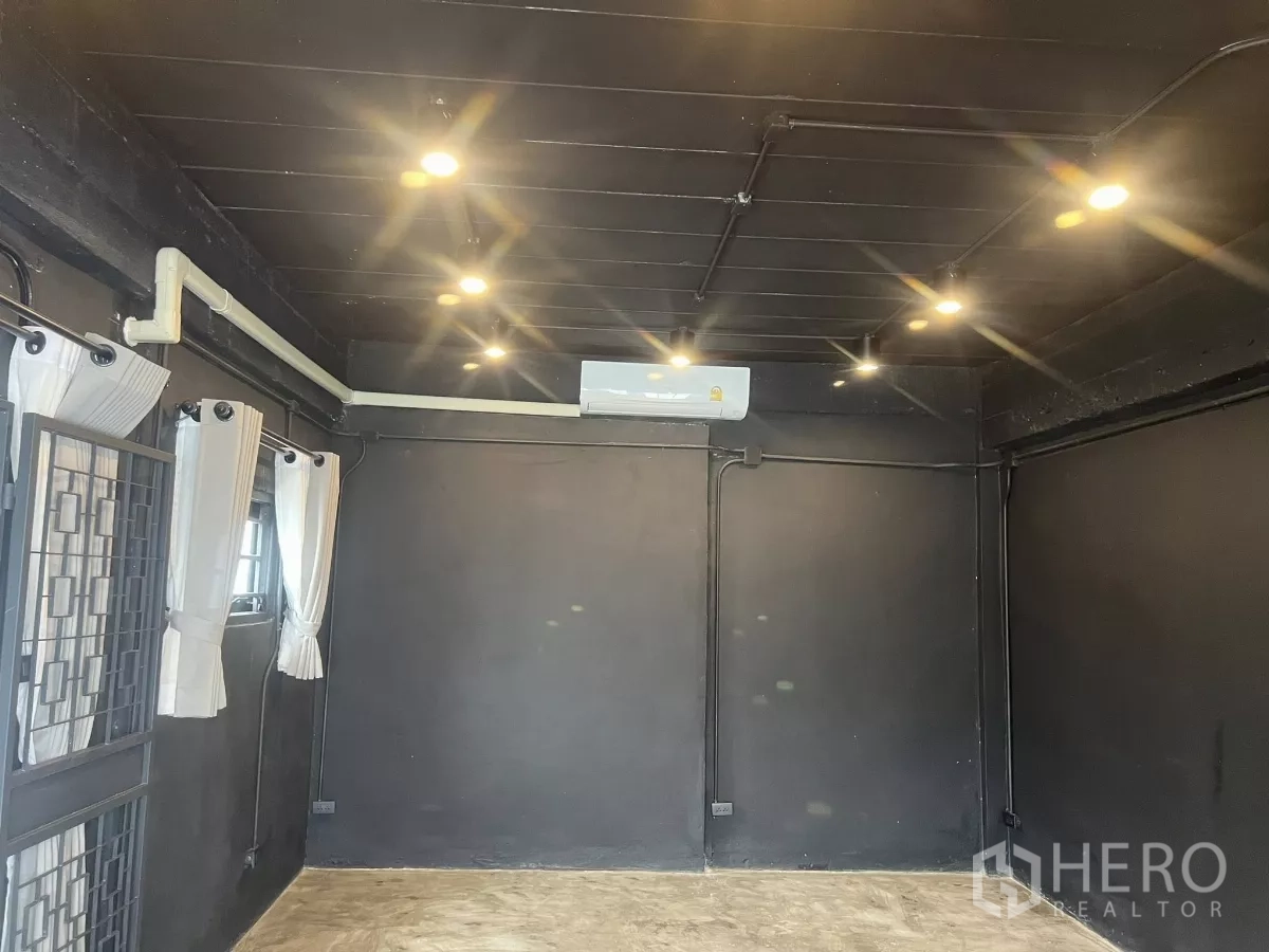Home Office for rent in Wang Thonglang, Bangkok - Studio-style room with black walls, spotlights, air conditioner, and curtained windows.