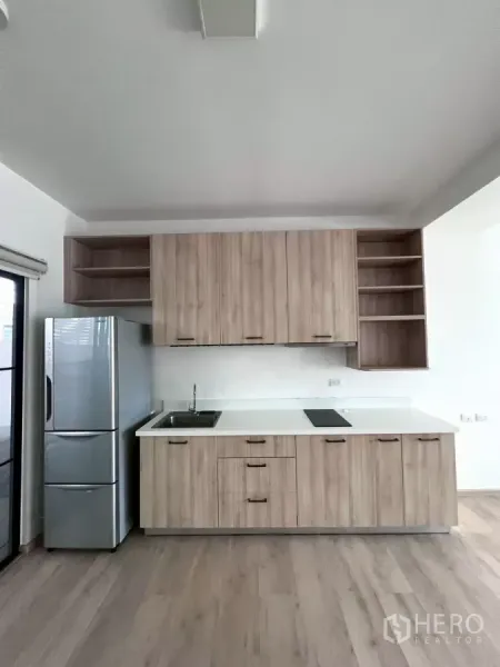 Townhouse for rent in Bang Phli, Samut Prakan - Compact kitchen with wood cabinetry, white countertop, cooktop, and stainless fridge.