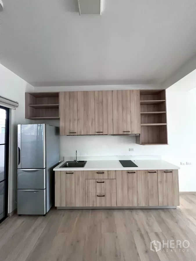 Townhouse for rent in Bang Phli, Samut Prakan - Compact kitchen with wood cabinetry, white countertop, cooktop, and stainless fridge.