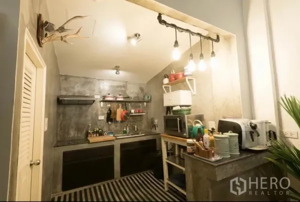Townhouse for rent in Khlong Toei, Bangkok - Industrial-style kitchen with concrete counters, open shelving and pendant lighting.
