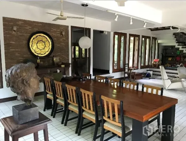 Detached House for rent in Khlong Toei, Bangkok - Large dining room with a long wooden table, brick feature wall, and ceiling track lights.