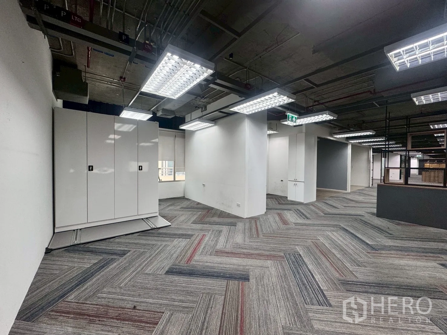 Office Space for rent in Watthana, Bangkok - Workspace with herringbone carpet, exposed ceiling, and white storage cabinets near the window.