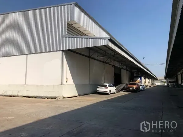 Warehouse for rent in Bang Phli, Samut Prakan - Exterior of warehouse with covered loading bay, raised dock and parking for trucks and cars.