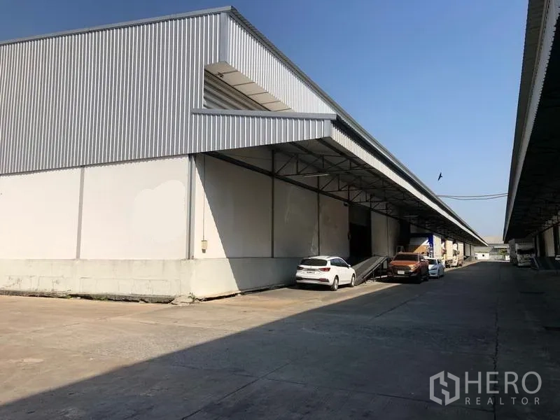 Warehouse for rent in Bang Phli, Samut Prakan - Exterior of warehouse with covered loading bay, raised dock and parking for trucks and cars.