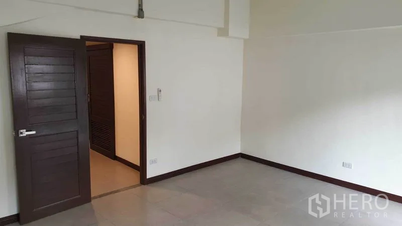 Townhouse for rent or sale in Khlong Toei, Bangkok - Spacious bedroom with wooden door and neutral tiled floors.