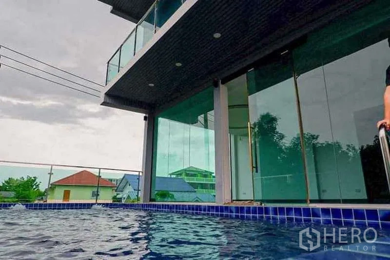Detached House for sale in Lat Phrao, Bangkok - Pool-level perspective of the home’s glass facade and balcony above.