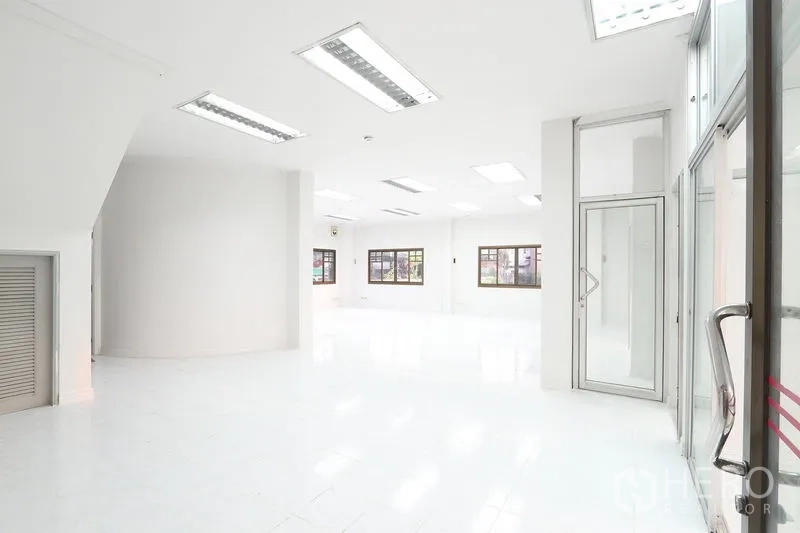 Office Space for rent in Bang Na, Bangkok - White ground‑floor office area with large windows, fluorescent lighting and a glass entry door.