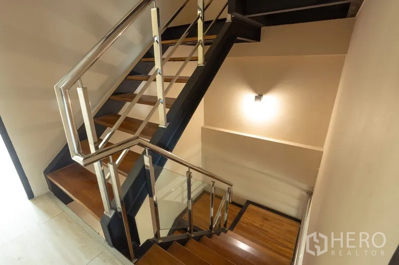Home Office for rent in Bang Khen, Bangkok - Interior stairwell showing sturdy metal handrails and warm wall lighting.