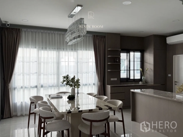 Detached House for rent or sale in Bang Phli, Samut Prakan - Bright dining room with crystal chandelier, marble table and upholstered chairs beside a sleek open kitchen in a Bang Phli detached house.