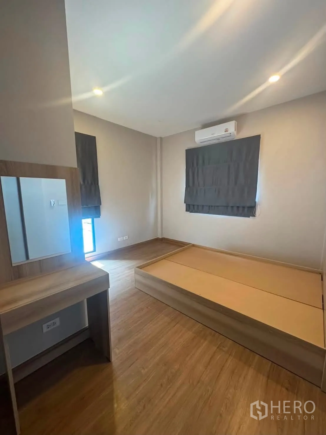 Detached House for rent or sale in Prawet, Bangkok - Cozy bedroom with platform bed, dressing table, wood flooring, window blinds, and AC.