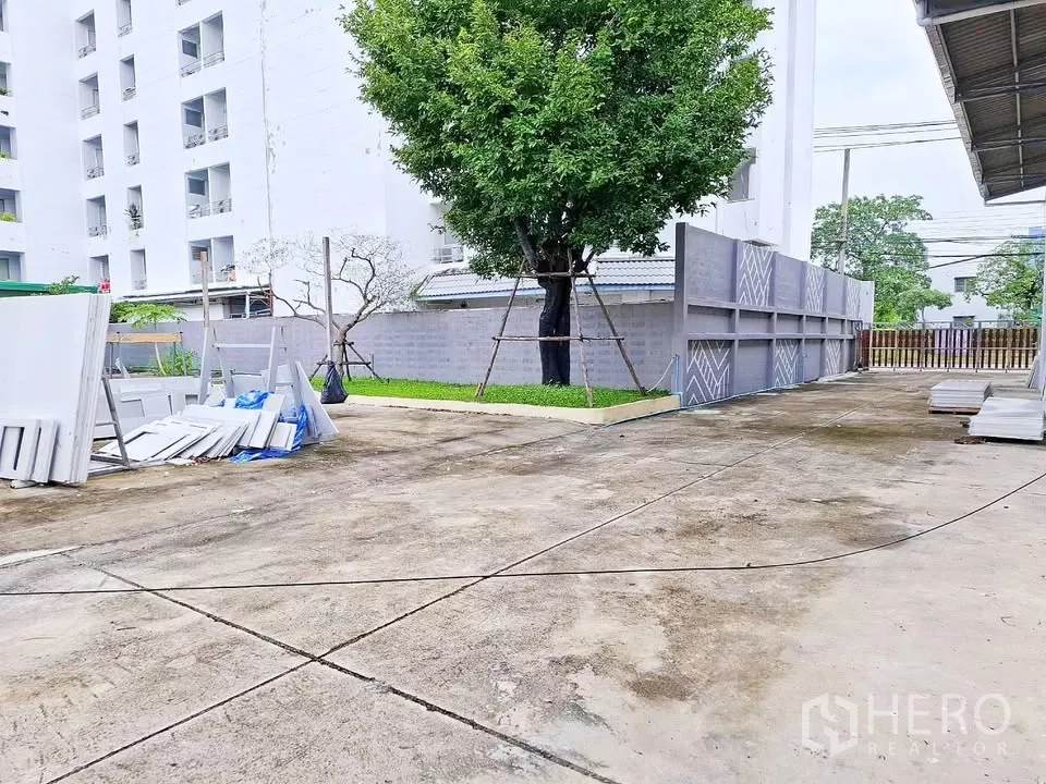 Warehouse for rent in Bang Kapi, Bangkok - Spacious concrete yard beside the warehouse with perimeter wall and a mature shade tree for parking and loading.