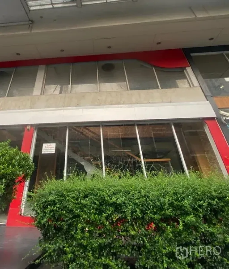 Retail Space for rent in Pathum Wan, Bangkok - Street-level retail facade with large glass windows, red trim and a hedge.